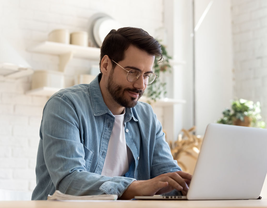 focused young man wearing glasses using laptop, typing on keyboard